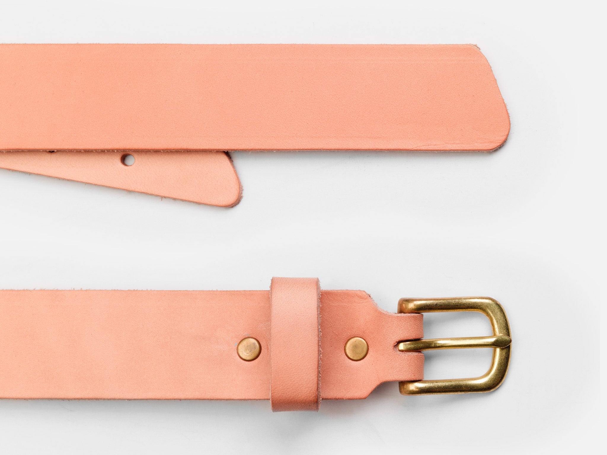 A close-up of a light pink leather belt with a brass buckle, shown laid flat on a white background. One end features the buckle and belt loop; the other end is pointed with holes for fastening.